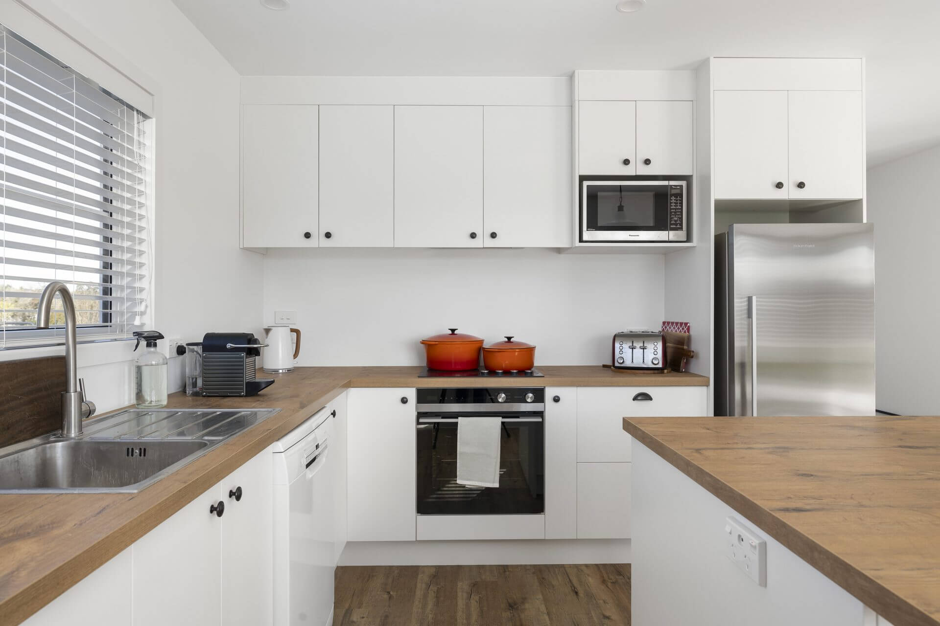 Renovated kitchen with white cabinetry wooden Benchtops and island and wooden floor floors
